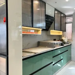 A work-in-progress shot of a modern kitchen with glossy green base cabinets and fluted glass upper cabinets. The black profile handles and under-cabinet lighting add a touch of elegance.