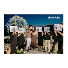 A creative group shot where friends and family hold up newspapers to announce the couple's engagement, with the couple sharing a kiss in the center.