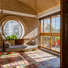 Sunlight filters through the circular pivot window, casting beautiful patterns across the floor and highlighting the craftsmanship of the teak and rattan swing.