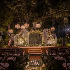 This stunning engagement stage was set under a canopy of trees, with chandeliers hanging like stars. The centerpiece is a modern, white slatted structure, with a floral arch creating a focal point for the couple's ceremony.
