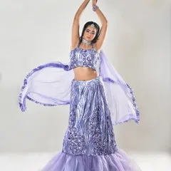 A full-length shot of a model in a sparkling lavender lehenga, perfect for an engagement or sangeet. The makeup is glamorous with a defined eye and a soft lip color to match the outfit.