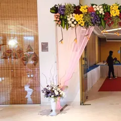 This entrance decor was for a corporate event. A colorful floral arrangement above the door and a vase of fresh flowers at the entrance create a professional and welcoming ambiance for attendees.