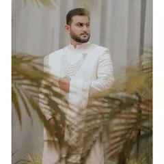 Elegance captured. This groom wears a custom all-white sherwani, featuring intricate chikankari work and layered pearl necklaces, creating a look of serene royalty for his special day.