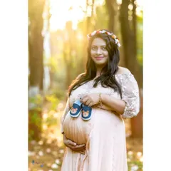 A serene solo portrait captured during the magical golden hour. The warm, soft sunlight beautifully highlights the mother's glow as she holds a pair of baby shoes, looking forward to the new chapter ahead.