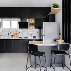 For a bold, modern look, this kitchen features all-black cabinetry. A patterned tile backsplash adds a graphic element, while a simple wooden shelf provides a touch of warmth and a place for everyday items. The island doubles as a breakfast bar.
