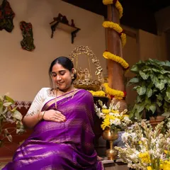A quiet moment of connection as a mother-to-be gently holds her belly, seated in a traditional South Indian home setting.