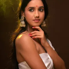 A warm, moody portrait with a focus on traditional jewelry. The soft, golden light highlights the intricate details of the jhumkas and nose ring, creating a classic and ethereal look.