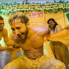 The fun continues as the groom's friends pull at his clothes, a classic playful moment during a lively Haldi ceremony.