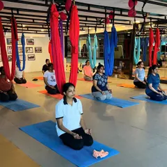A moment of calm before our aerial yoga class begins. Students are centered in Vajrasana (Thunderbolt Pose) on their mats, with the colorful aerial silks hanging above, ready for practice.