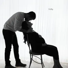 An intimate backlit silhouette of a couple sharing a tender kiss. The soft light from the window creates a dreamy and romantic atmosphere, focusing on their connection.