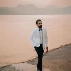 A dapper groom by the lakeside at dusk. This portrait has a cool, cinematic feel, like a still from a classic movie.