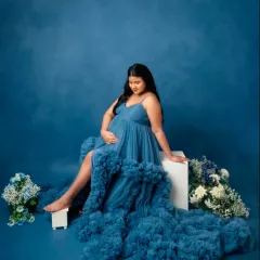 Seated gracefully, this pose highlights the texture and volume of the blue tulle gown. The high-low hem and flowing train add a touch of modern royalty to your pregnancy photoshoot.