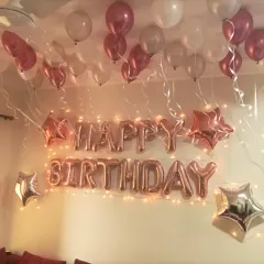 A classic and simple room decoration for a birthday surprise. Rose gold "Happy Birthday" foil letters, star-shaped foils, and balloons floating on the ceiling create a festive and celebratory feel.