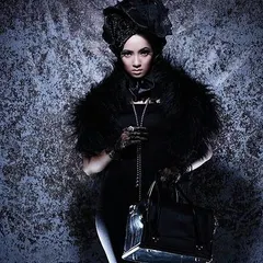 A dark, gothic-inspired fashion look. The makeup is intense and dramatic, with heavily defined eyes and pale skin to create a high-contrast, vintage couture style.