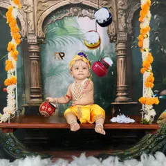 A beautiful portrait of a baby as Little Krishna, sitting on an ornate swing decorated with marigolds and peacocks. This elaborate setup creates a majestic and timeless image.