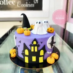 A spooky and fun Halloween cake with a haunted house silhouette, ghosts, and pumpkins.