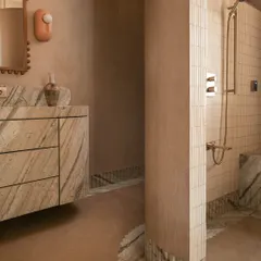 We call this bathroom a 'chic desert dream'. It features blush-toned micro-concrete walls and a monolithic vanity carved from veined Corteccia marble. The stone appears to trickle down onto the floor, creating a fluted skirting detail that is both organic and luxurious.