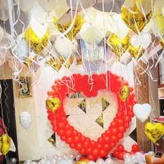 A room filled with love for a birthday surprise. This decoration features a large heart-shaped balloon frame, with dozens of white and gold heart-shaped foil balloons floating from the ceiling.