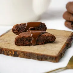 A soft chocolate cookie broken in half with chocolate sauce drizzled on top, emphasizing its gooey texture.