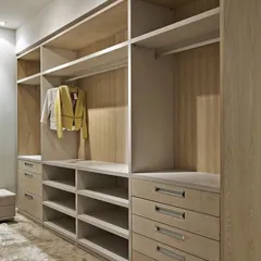 This open-concept walk-in closet uses a light wood finish to create a bright and airy feel. The design includes a mix of drawers with premium metal handles, open shelves, and dedicated sections for long and short garments.