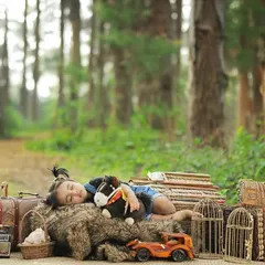 A one-year-old girl takes a nap amidst vintage props during her outdoor photoshoot in a serene, wooded area.