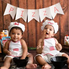 A fun twin photoshoot with a "Pizza Kitchen" theme, where two babies are dressed as little chefs.