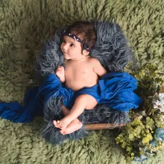 A beautiful color combination of royal blue and green makes this baby portrait pop. The baby is propped up in a basket, looking off to the side with a curious expression.