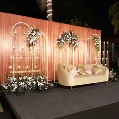 We designed this sophisticated reception stage with a rose-gold sequin backdrop, framed by modern white arches and accented with floral bouquets. The curved lounge seating adds a contemporary and comfortable touch for the couple.
