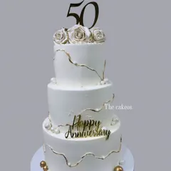 A stunning three-tier eggless cake created to celebrate a golden 50th anniversary. The design features elegant white fondant with delicate gold kintsugi-style cracks, pearls, and handcrafted sugar roses, perfect for a landmark celebration.