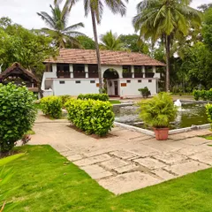 Our pathways are designed for peaceful wandering. This view shows a stone path leading past our serene lotus pond towards a heritage building, surrounded by the lush greenery that thrives in the pre-monsoon calm.