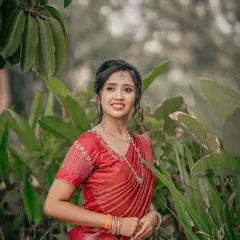 A candid portrait of a bride in a vibrant red saree, captured in a natural outdoor setting.