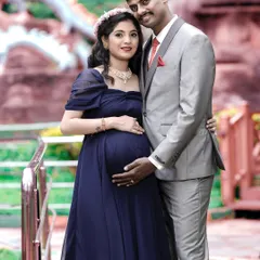 A formal and elegant couple's portrait. The coordinated outfits and classic pose by the railing result in a sophisticated and timeless image celebrating their pregnancy.