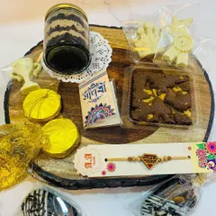 Here are the contents of the Rakhi hamper displayed, showing the variety of treats you get. The hamper includes double chocolate cakesicles, a jar cake, Rasmalai chocolates, dry fruit mendiants, a brownie, and a rakhi with traditional accompaniments.