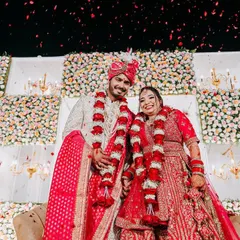 A beautiful Varmala moment. The couple exchanges garlands in front of a surreal backdrop of alternating white floral panels and elegant chandeliers.