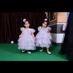 The twin girls stand together in their matching lavender birthday dresses. The design is comfortable for them to move and play in while looking picture-perfect for their special day.