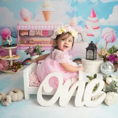 This little girl sits on a miniature bed as part of her Candyland-themed first birthday shoot, looking like a princess in her sweet kingdom.