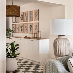 A view from the living room into the foyer, where a long console provides ample storage. The gallery wall of botanical prints and a large woven pendant light introduce the home's modern coastal theme.