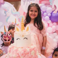 The birthday girl, Maseera, smiling brightly next to her adorable unicorn-themed cake. Her happiness is the real magic.