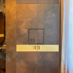 This shot highlights the floor-to-ceiling wardrobe with its unique metallic-finish laminate and fluted wood panel at the top. The horizontal gold handle is not just hardware; it's a central design element.