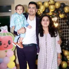 A posed family photo at a child's birthday party, with a festive black and gold balloon arch in the background.