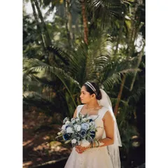 A beautiful bridal portrait against a lush, green background. The warm sunlight highlights the bride's features and the details of her dress and bouquet.