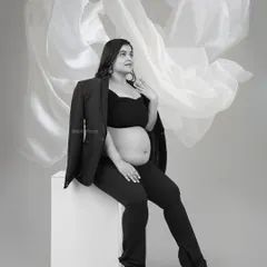 A high-fashion, monochrome look with a black pantsuit and blazer draped over the shoulders, showcasing a bold and stylish pregnancy portrait.