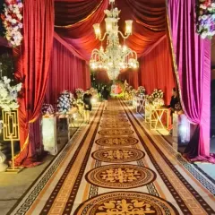 A royal entrance corridor with rich magenta draping, a patterned carpet, and a series of magnificent crystal chandeliers leading the way to the main event.