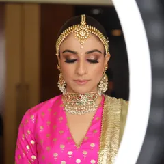 A serene moment as the bride gets her makeup done. The ring light creates a beautiful, soft glow, highlighting her stunning jewelry and the artist's work.