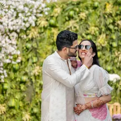 A candid moment from a Haldi ceremony, where the couple shares a playful and affectionate look against a backdrop of white flowers and greenery.
