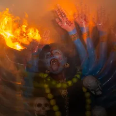 The raw energy of Kulasai Dasara captured in a motion-blurred image of a devotee as Kali, surrounded by fire. The swirling colors and light convey the intensity of the trance-like performance.