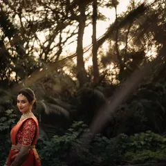 A stunning bridal portrait taken in a forest during the golden hour. The warm light filtering through the trees creates a magical, ethereal glow around her.