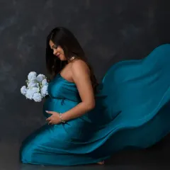 A goddess in teal. This portrait uses a flowing satin drape to create a sense of movement and elegance, highlighting the beautiful silhouette of the baby bump.