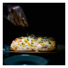 A chef adds a final garnish of cheese to a freshly prepared flatbread pizza. The dramatic lighting and dark background highlight the dish, making it look irresistible.