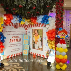 A personalized photo corner at a carnival-themed party, including a large framed picture of the birthday boy and a custom "Welcome Anamay" message board.